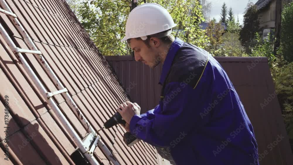 The worker repairs the ladder on the roof using a wireless drill 4k. The worker repairs the ladder on the roof using a wireless drill 4k.