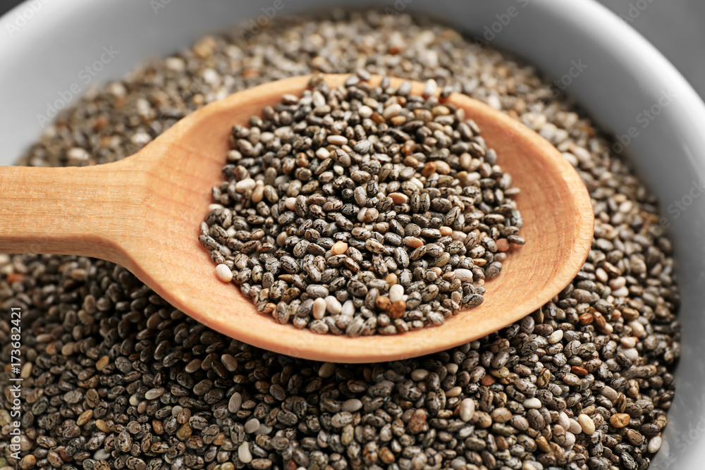 Chia seeds in wooden spoon over bowl, closeup Chia seeds in wooden spoon over bowl, closeup
