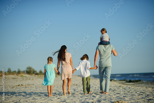 Big happy family walking at the beach. Mom, dad and three children. The blue sky, the sun, fresh sea wind. Pleasure from nature and communication.