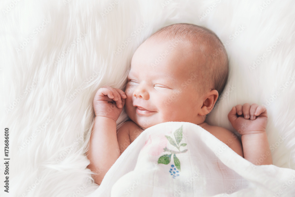 © nataliaderiabina - Sleeping smiling newborn baby in a wrap on white blanket.
