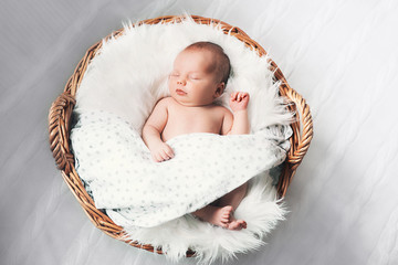 Sleeping newborn baby in a wrap on white blanket.