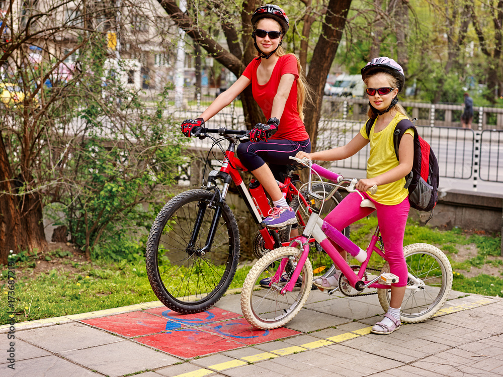 Obraz premium Family bike ride in autumn. Mother and daughter wearing bicycle helmet with rucksack. Children biking on yellow bike lane. Child in foreground teenager on background. Children travel unaccompanied.