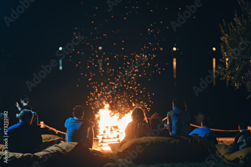 Schilderij op canvas Group of people near camp fire with campfire song and campfire meals playing campfire games and eating campfire grill, telling campfire stories near the fire with wood, flames in the nature at night