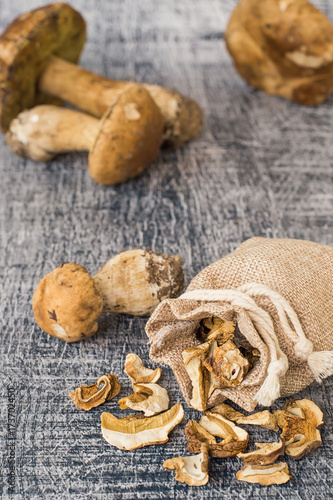  A small linen sack with cut dried mushrooms and fresh whole mushrooms on a wooden background.