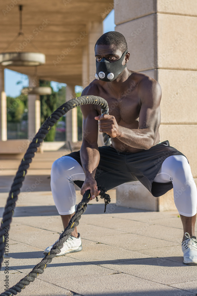 male muscular training with battle ropes and training mask