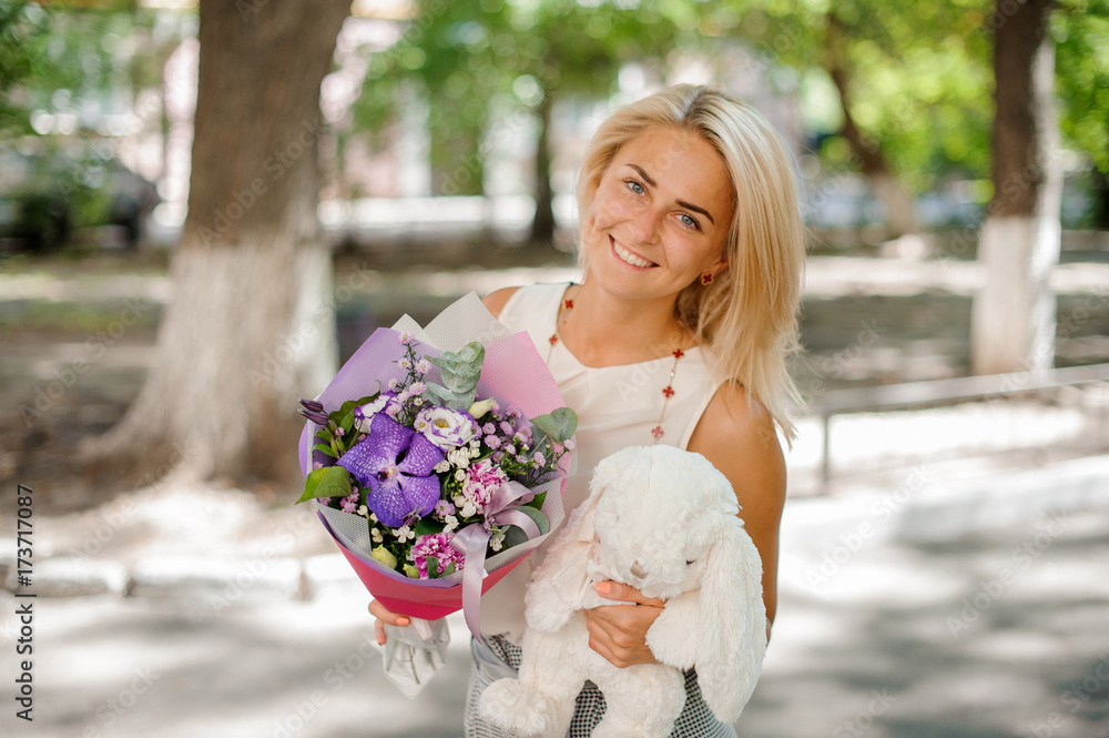 Fototapeta premium Smiling woman holding a pretty composition of flowers and toy