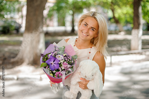Smiling woman holding a pretty composition of flowers and toy