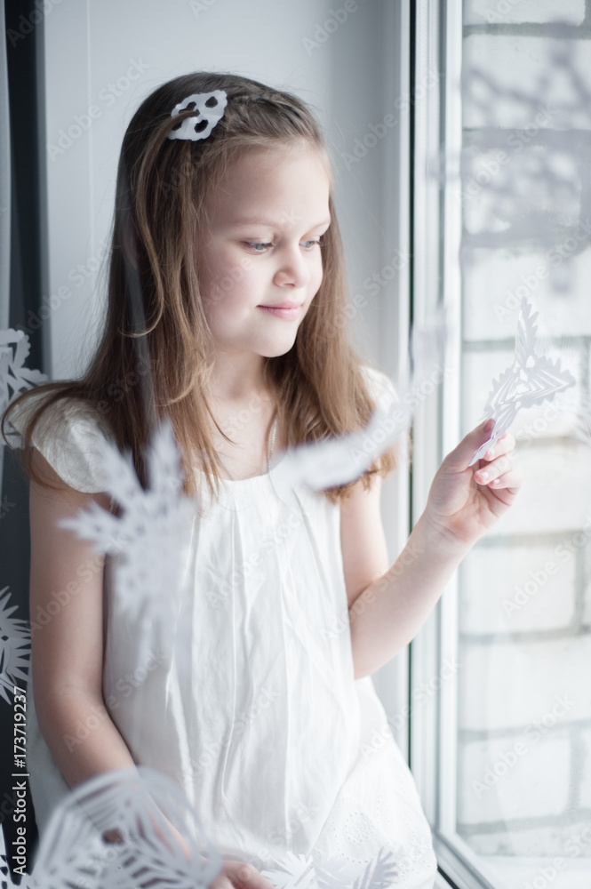girl in white dress sits on window sill among snowflakes and looks out the window girl in white dress sits on window sill among snowflakes and looks out the window