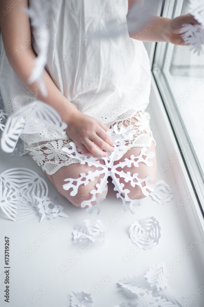A white snowflake of paper lies on the lap of a girl