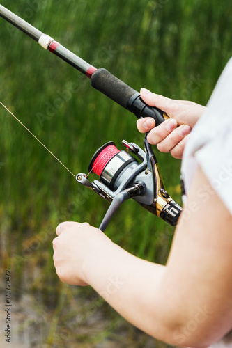 female hands holding a fishing rod and twist the handle of the fishing reel. Shallow depth of field, soft focus