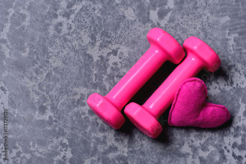 Dumbbells made of pink plastic near soft toy heart photo