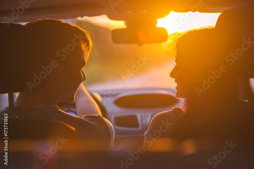 The happy couple sitting in a car on the background of the sunset