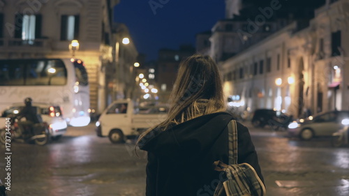 Fotografie Young traveling woman with backpack crossing the traffic road, tourist looking around and find the way in the evening