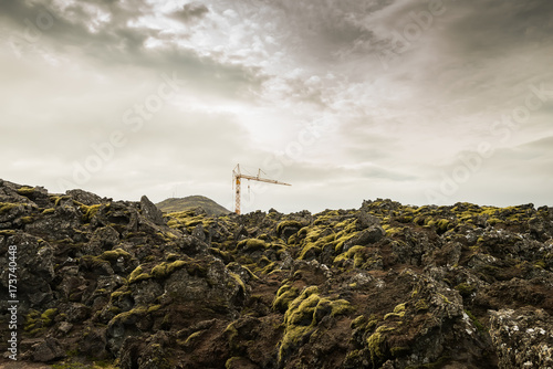 Lifting construction crane among the rocky terrain covered with lava and moss. Iceland. Construction in hard-to-reach places.

