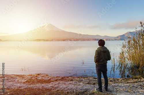 Asian man traveler looking sunrise and mount fuji reflect on water in morning at kawaguchiko lake japan