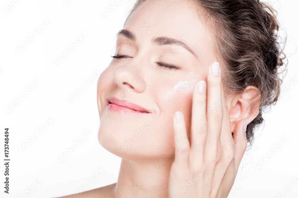 Beautiful young woman smiling and applying eye cream.