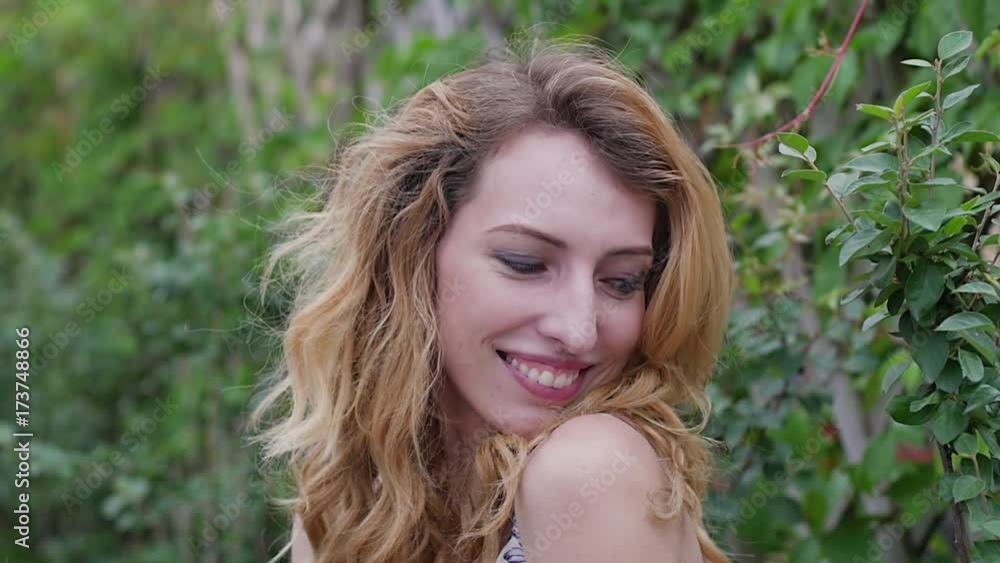 beautiful young woman sits on a green hedge background. slow motion. urban summer landscapes beautiful young woman sits on a green hedge background. slow motion. urban summer landscapes