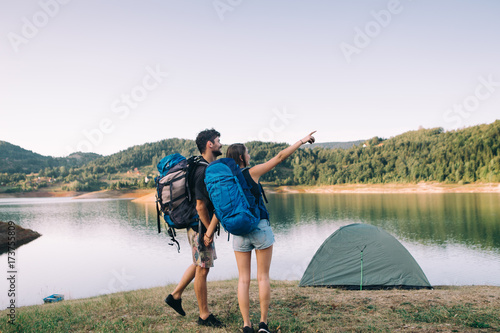 Hiking couple. Young couple with backpacks holding hands beside lake 