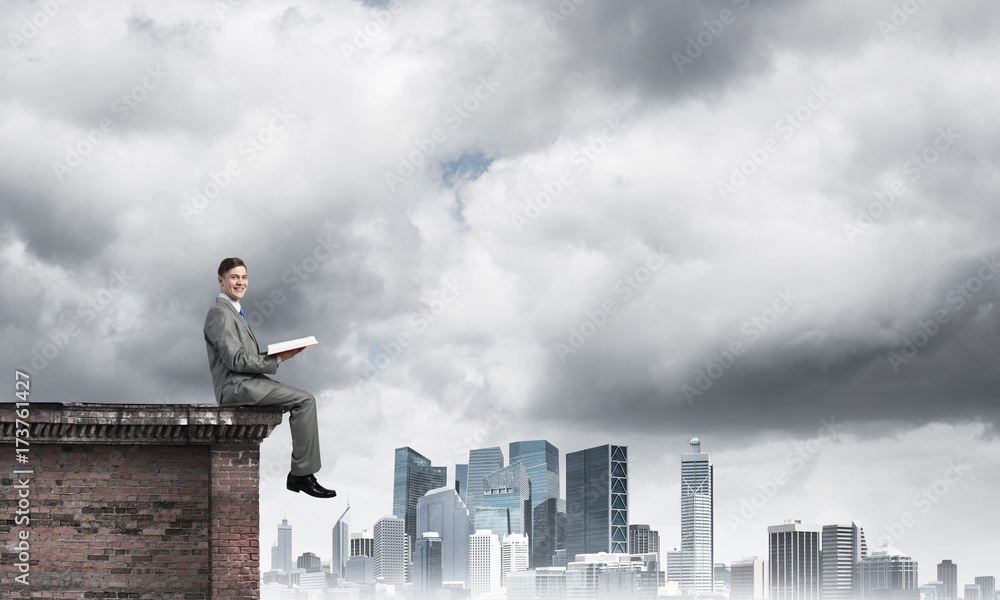 Man on roof edge reading book and cityscape at background Man on roof edge reading book and cityscape at background