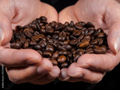 Womens hand with coffee beans with black background over wooden table