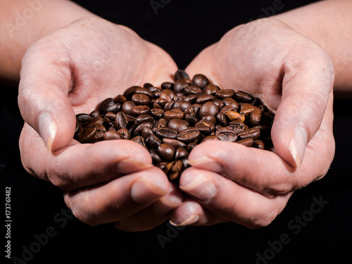 Womens hand with coffee beans with black background over wooden table