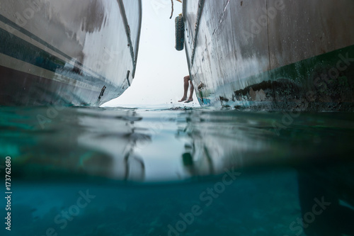 In the sea there are two yachts and from the side are visible the legs of a man. View half under water