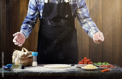 man in an apron preparing a pizza, knead the dough and puts ingredients