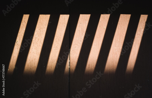 shade from wooden lath window which causes shadow and light to wood floor.