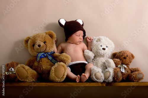Newborn baby boy wearing a brown knitted bear hat and pants, sleeping on a shelf