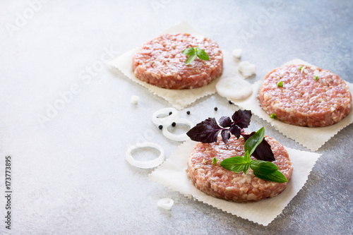 Raw hamburgers - cutlets from organic beef meat with spices and basil on a stone or slate background, top view with copy space.