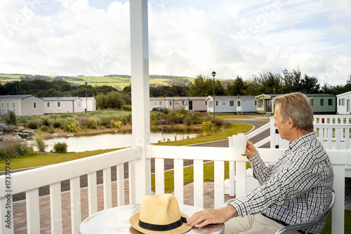 Elderly man drinking a mug of coffee sitting on the veranda of a luxury static caravan in North Wales UK.