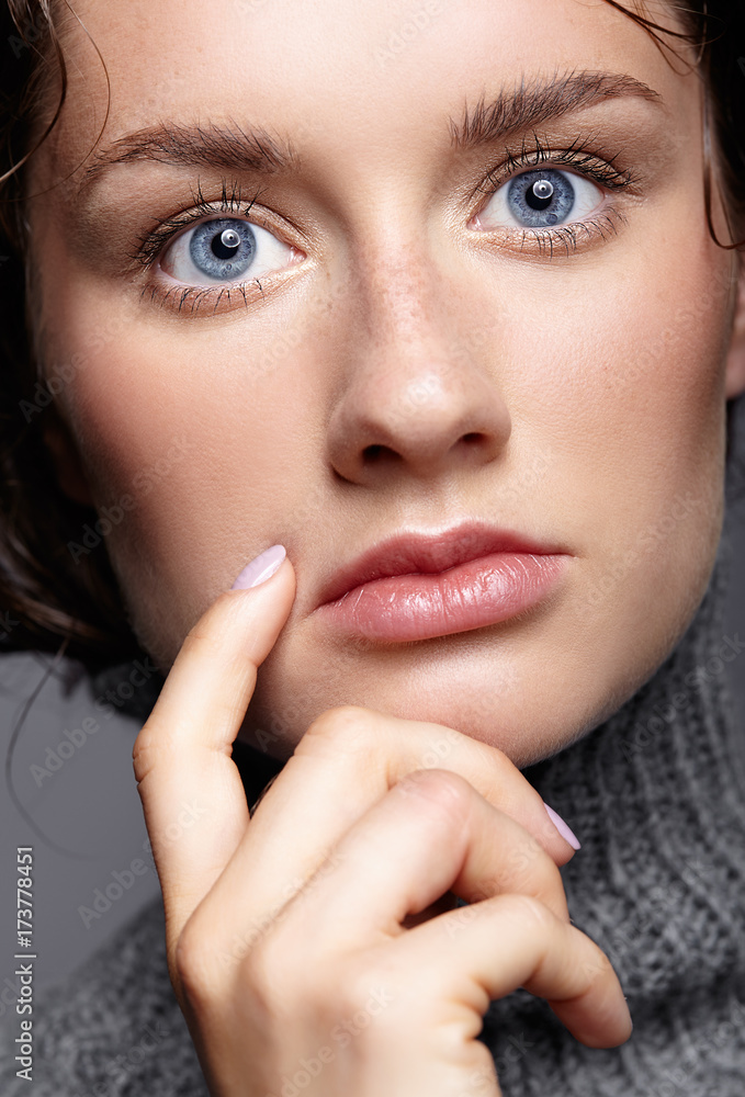 Beauty portrait of young woman in gray wool sweater. Brunette girl with bright blue eyes and day female makeup Beauty portrait of young woman in gray wool sweater. Brunette girl with bright blue eyes and day female makeup