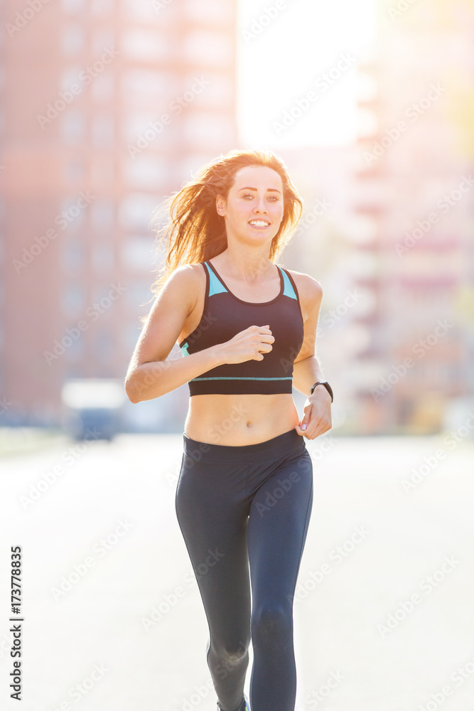 Young smiling sporty woman running on road street in the morning. Fitness girl jogging in city