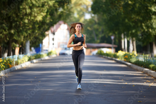 Young smiling sporty woman running on the road in the morning. Fitness girl jogging in park © skumer
