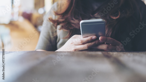 Closeup image of a woman's hands holding and using at smart phone on wooden table in vintage cafe