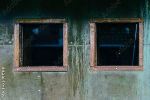 Two copper-trimmed square windows on a verdigris wall photo