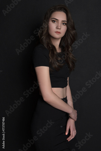brunette girl in black clothes standing looking at camera black background