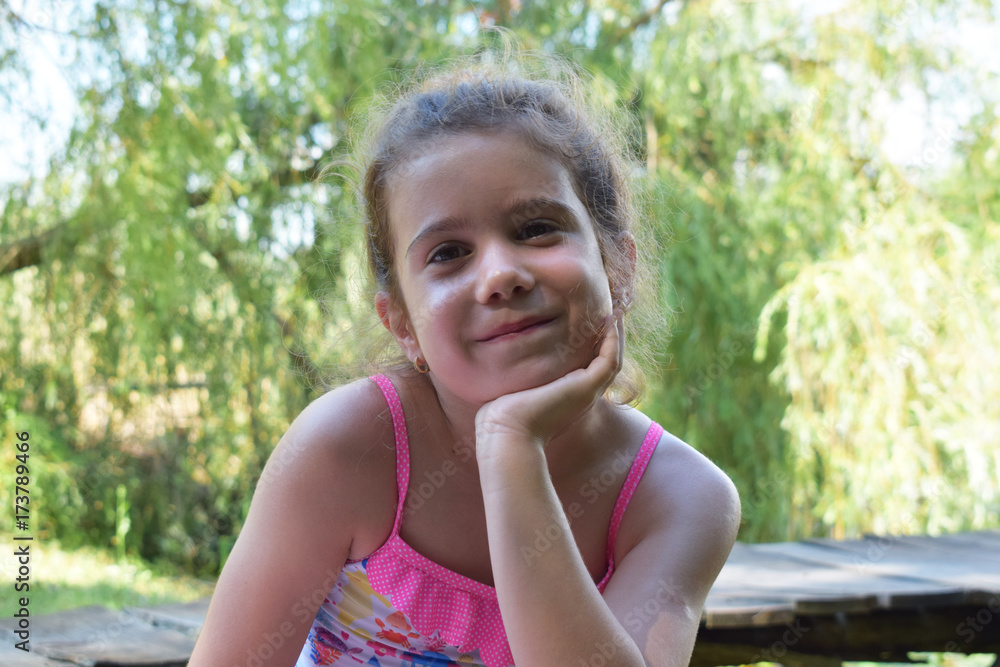 Smiling little girl with head in her hand enjoying a day in nature and looking at camera.