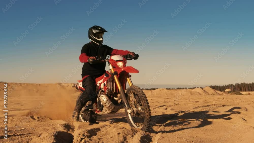 Professional FMX Motorcycle Rider Twists Full Throttle Handle and Starts Riding on the Sandy Off-Road Track. Scenic Sunset. Shot on RED EPIC-W 8K Helium Cinema Camera. Professional FMX Motorcycle Rider Twists Full Throttle Handle and Starts Riding on the Sandy Off-Road Track. Scenic Sunset. Shot on RED EPIC-W 8K Helium Cinema Camera.
