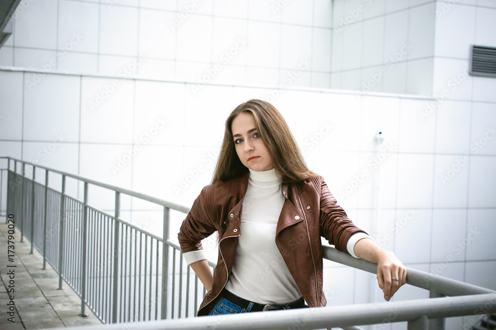 Fototapeta premium street portrait of a female student in fashionable clothes, blue jeans and a brown jacket, outdoors