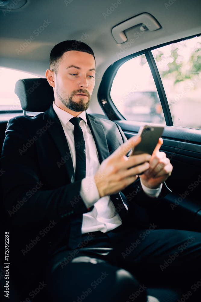 A businessman while traveling by car in the back seat, send a message or email and calls. The man in the driver career for his business trips.
