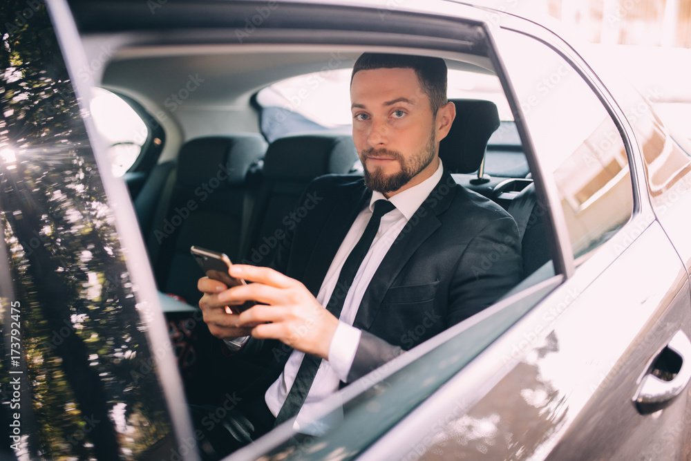 Businessman talking on the mobile phone and looking outside the window while sitting on back seat of a taxi. Male business executive travelling by a car and making phone call.