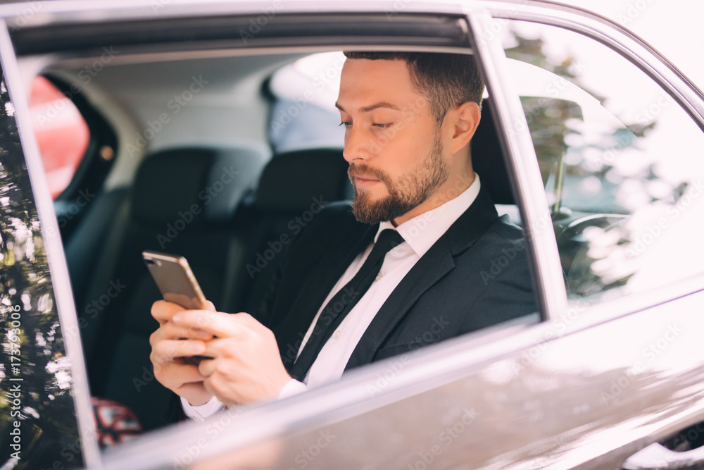 Businessman talking on the mobile phone and looking outside the window while sitting on back seat car