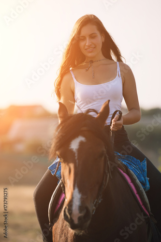 Beautiful young cowgirl riding her horse in field
