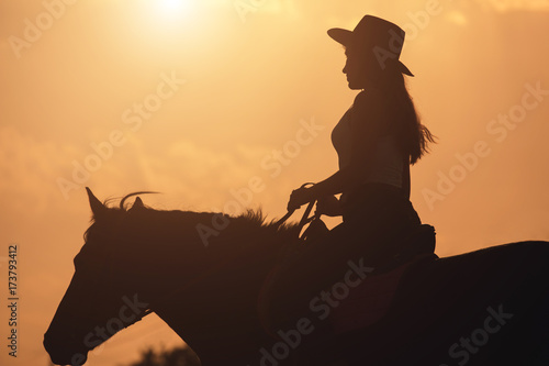 Sunset silhouette of young cowgirl riding her horse photo