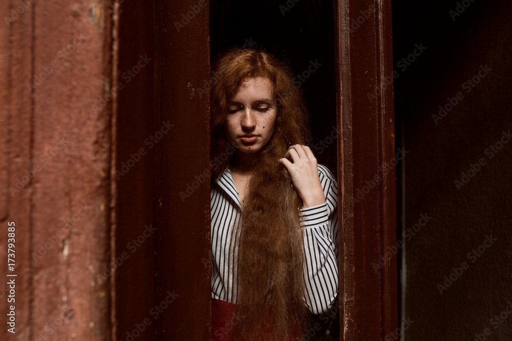 Sad red haired model standing behind a closed glass door. Raindrops on the glass Sad red haired model standing behind a closed glass door. Raindrops on the glass
