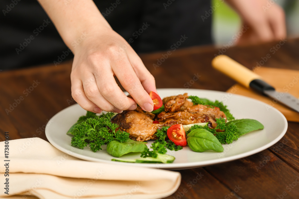 Woman decorating chicken dish with vegetables in kitchen