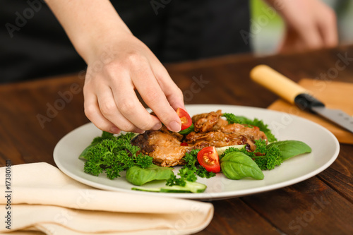 Woman decorating chicken dish with vegetables in kitchen