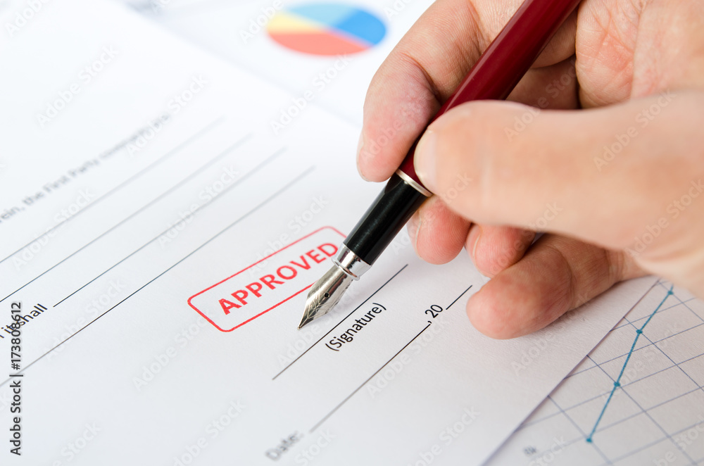 Man signs the contract with pen. Approved stamp on document Man signs the contract with pen. Approved stamp on document