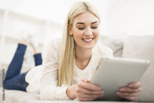 The smile woman lay on the sofa and hold a tablet